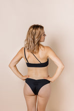 Load image into Gallery viewer, Girl in black bikini set. Top is asymmetrical with the straps coming up to the left shoulder. Back view