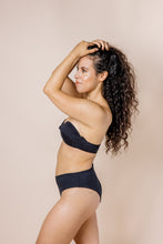 Load image into Gallery viewer, Girl in black bikini set. Bandeaux Top has off-shoulder sleeves. side shot
